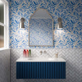 Bathroom featuring Liberty White 7.5x15cm rustic effect gloss wall tiles laid in a herringbone pattern, paired with blue botanical wallpaper, a navy fluted vanity unit, chrome wall lights and an arched mirror for a fresh, classic look.