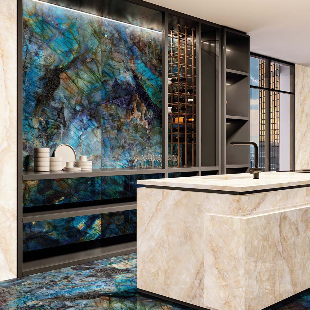 Luxury kitchen interior featuring Lumen Precious Stone Labradorite 60 × 120cm polished porcelain wall and floor tiles, showcasing dramatic blue, teal, and black gemstone-inspired tones with a high-gloss finish, paired with a marble-effect island and dark contemporary cabinetry.