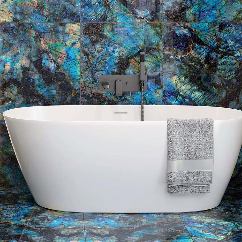 Bathroom interior featuring Lumen Precious Stone Labradorite 60 × 120cm polished porcelain wall and floor tiles, showcasing vivid blue, teal, and charcoal gemstone-inspired detailing with an iridescent high-gloss finish, paired with a freestanding white bath and brushed metal fittings for a dramatic luxury look.