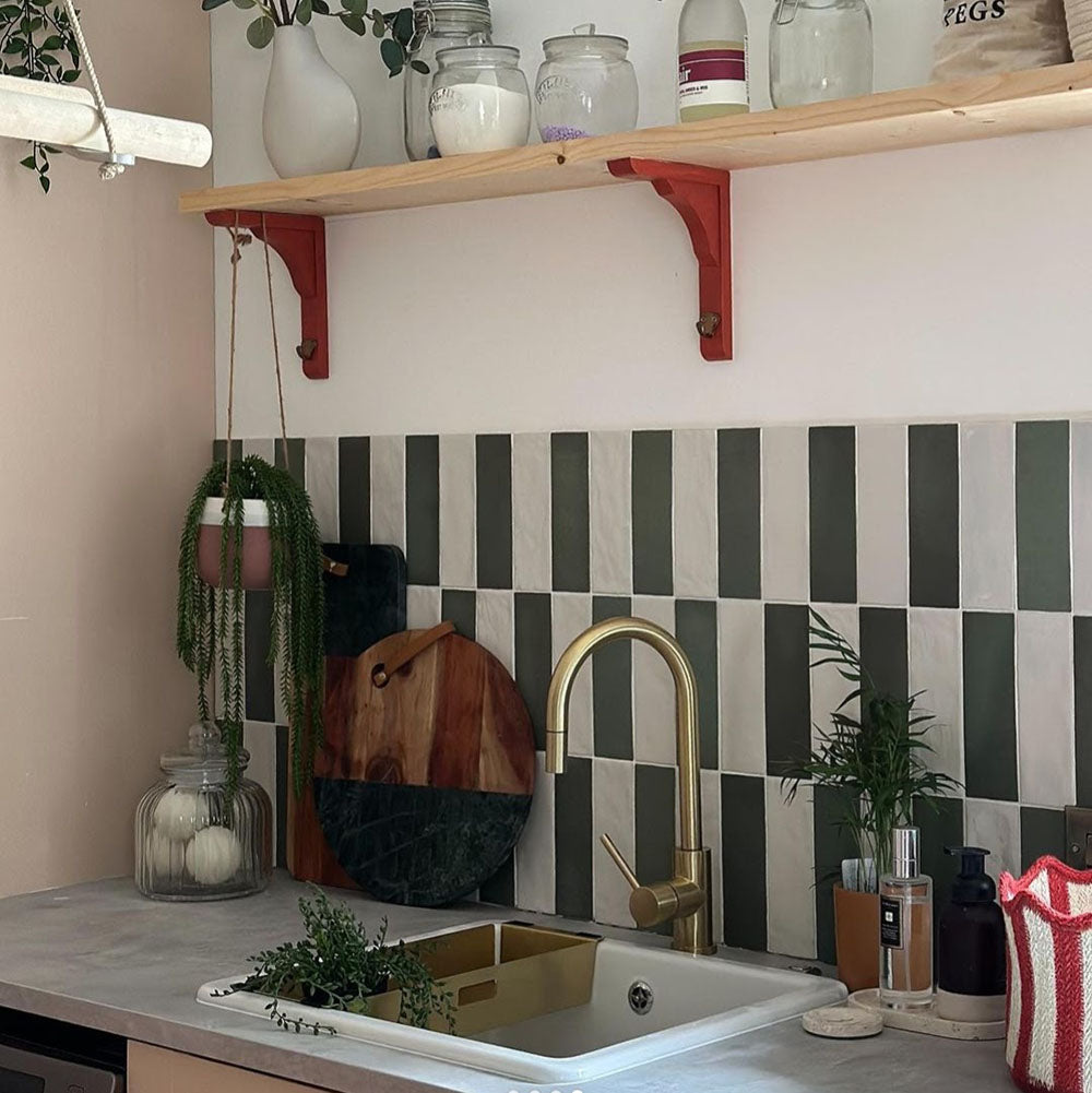 Kitchen interior featuring Zellige Malachite Green and Zellige Oyster 6.5x20cm Moroccan-style brick tiles installed vertically in a striped splashback, styled with brass tap, wooden shelving, and greenery for a warm, contemporary look.