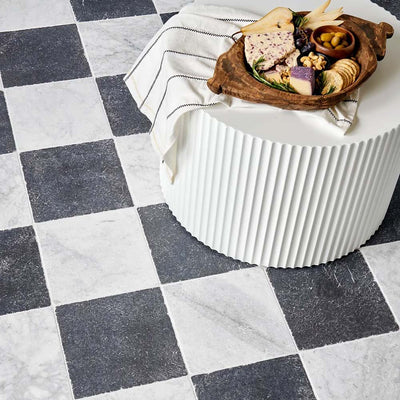 Interior setting featuring Fayrouz Black 15.2x15.2cm natural marble tiles with a tumbled finish, installed in a classic chequerboard layout with white marble, styled with a fluted table and decorative serving board.