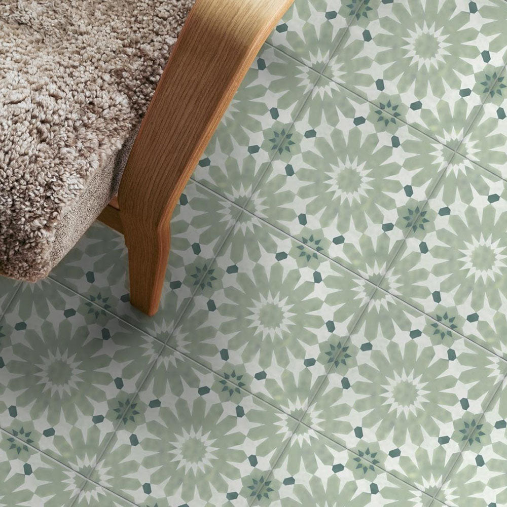 Living room floor featuring Fez Jade Green 20x20cm Moroccan-style porcelain tiles, showcasing a soft green geometric pattern, styled with a curved wooden chair and neutral textured upholstery for a warm, contemporary look.