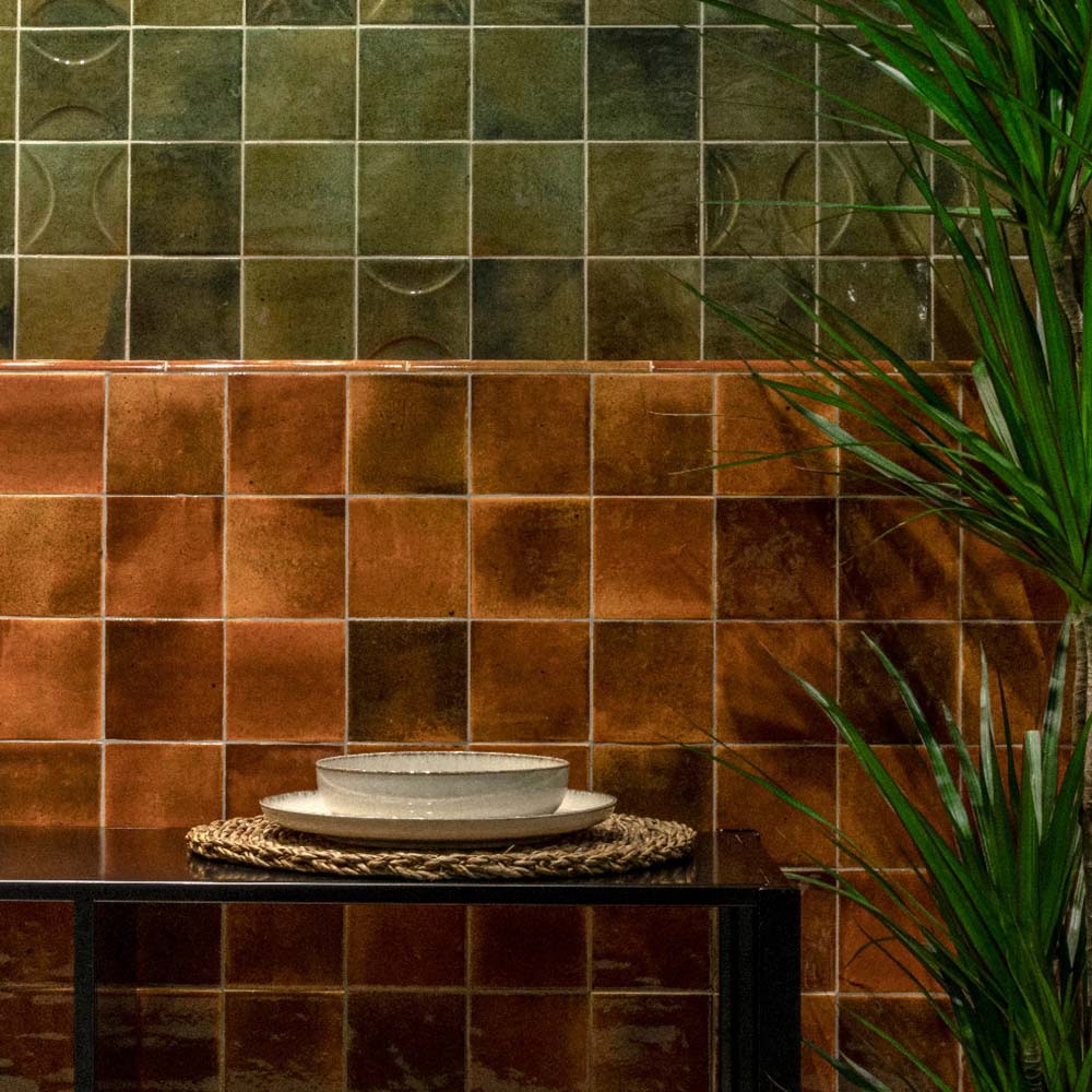 Interior detail featuring Saigon Amber Square Wall tiles in a Moroccan-inspired style, 10 × 10cm glossy ceramic tiles in warm amber tones, styled with layered tiles, greenery, and decorative tableware.