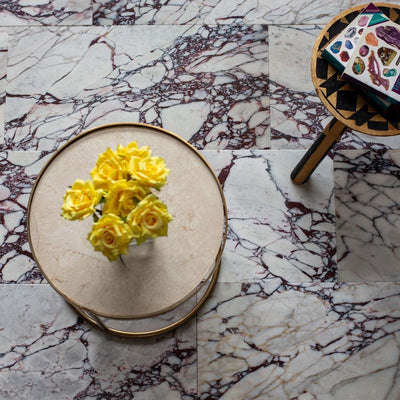 Interior setting featuring Fayrouz Viola 30.5x61cm natural marble tiles with a honed finish, installed in a staggered layout, showcasing a white base with striking burgundy veining, styled with a round table and decorative accessories.