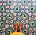 Floor featuring Fez Autumn 20x20cm Moroccan-style porcelain tiles, showcasing a rich geometric star pattern in earthy green, blue and blush pink tones, styled with tan leather sandals for a warm, bohemian look.
