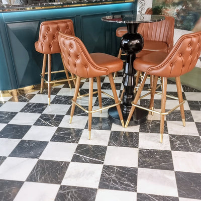 Interior setting featuring Fayrouz White 15.2x15.2cm natural marble tiles with a honed finish, installed in a classic chequerboard floor with black marble, styled with tan leather bar stools and a dark statement table.