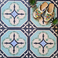 Flat-lay setting featuring London Streets Goodwin Court 20x20cm Victorian Moroccan style floor tiles, showcasing a soft blue, cream and charcoal geometric pattern, styled with decorative slippers and small plants for a lifestyle tile display.