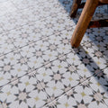 Marketing image of Agadir Natural Moroccan-style 20x20cm porcelain tiles laid on a floor, featuring a soft neutral geometric star pattern with subtle grey and warm beige tones, styled with a wooden chair for a lived-in look.