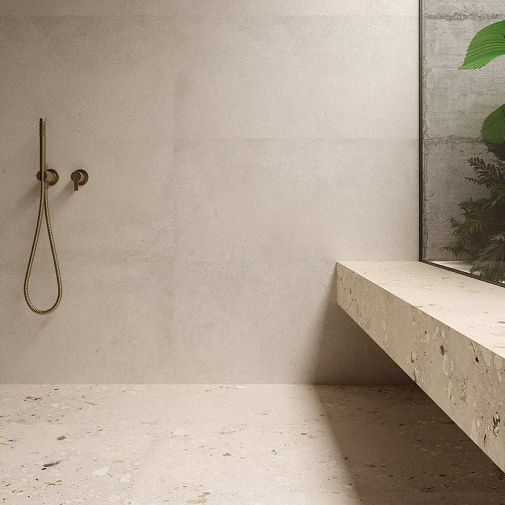 Minimalist bathroom featuring Melange Light concrete-style wall and floor tiles 60 × 60cm, showcasing soft beige concrete-effect tones with subtle texture, paired with terrazzo surfaces, brass fittings, and contemporary architectural styling.