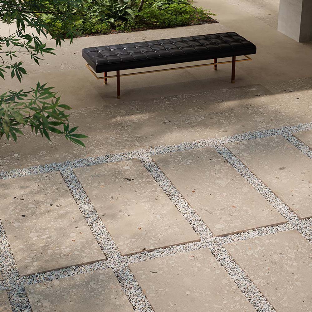 Modern outdoor seating area featuring Melange Sand 20mm thick outdoor Cosmo Stone tile slabs 60 × 120cm, showcasing warm sand-toned terrazzo-inspired detailing, paired with gravel pathways, contemporary landscaping, and minimalist outdoor furniture.