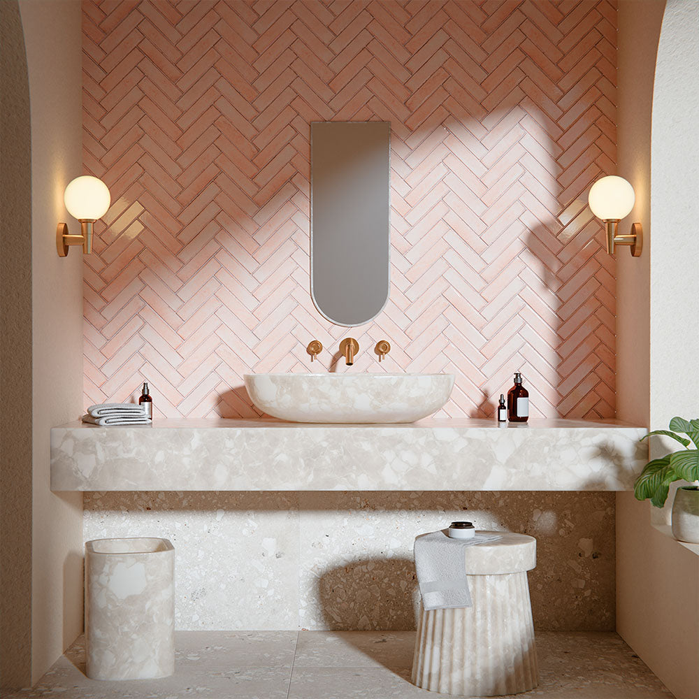 Contemporary bathroom featuring Melange Sand Cosmo Stone wall and floor tiles 60 × 120cm, showcasing warm sand-toned terrazzo-inspired detailing, paired with blush herringbone wall tiles, brass fittings, and marble-effect bathroom features.