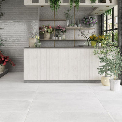 Bright botanical interior featuring Melody Cement White 30 × 60cm concrete-effect porcelain floor tiles, showcasing soft white tones and a subtle industrial texture, paired with natural wood finishes, layered greenery, and light-filled contemporary styling.
