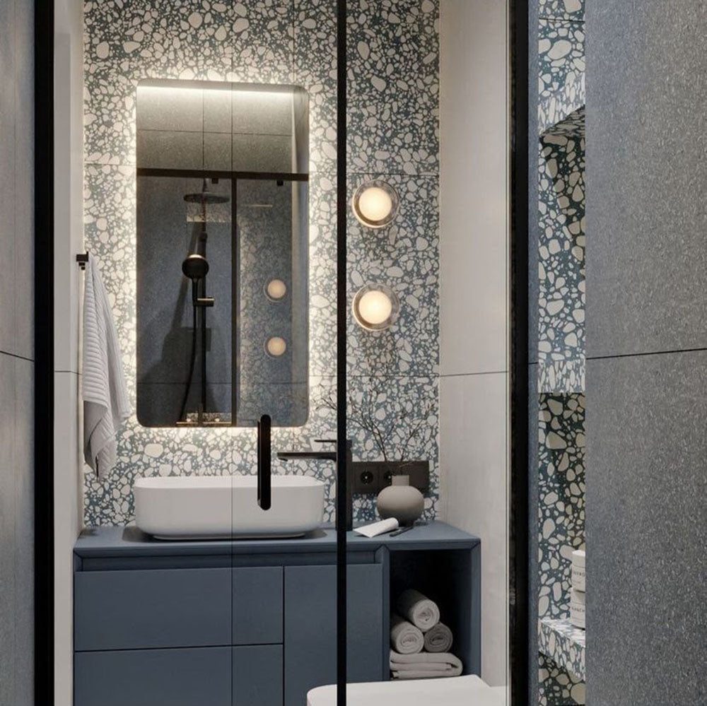 Modern bathroom featuring Melody Pop Blue 60cm x 120cm terrazzo effect porcelain feature wall tiles, paired with large-format grey wall tiles, a blue floating vanity, black brassware and illuminated mirror.
