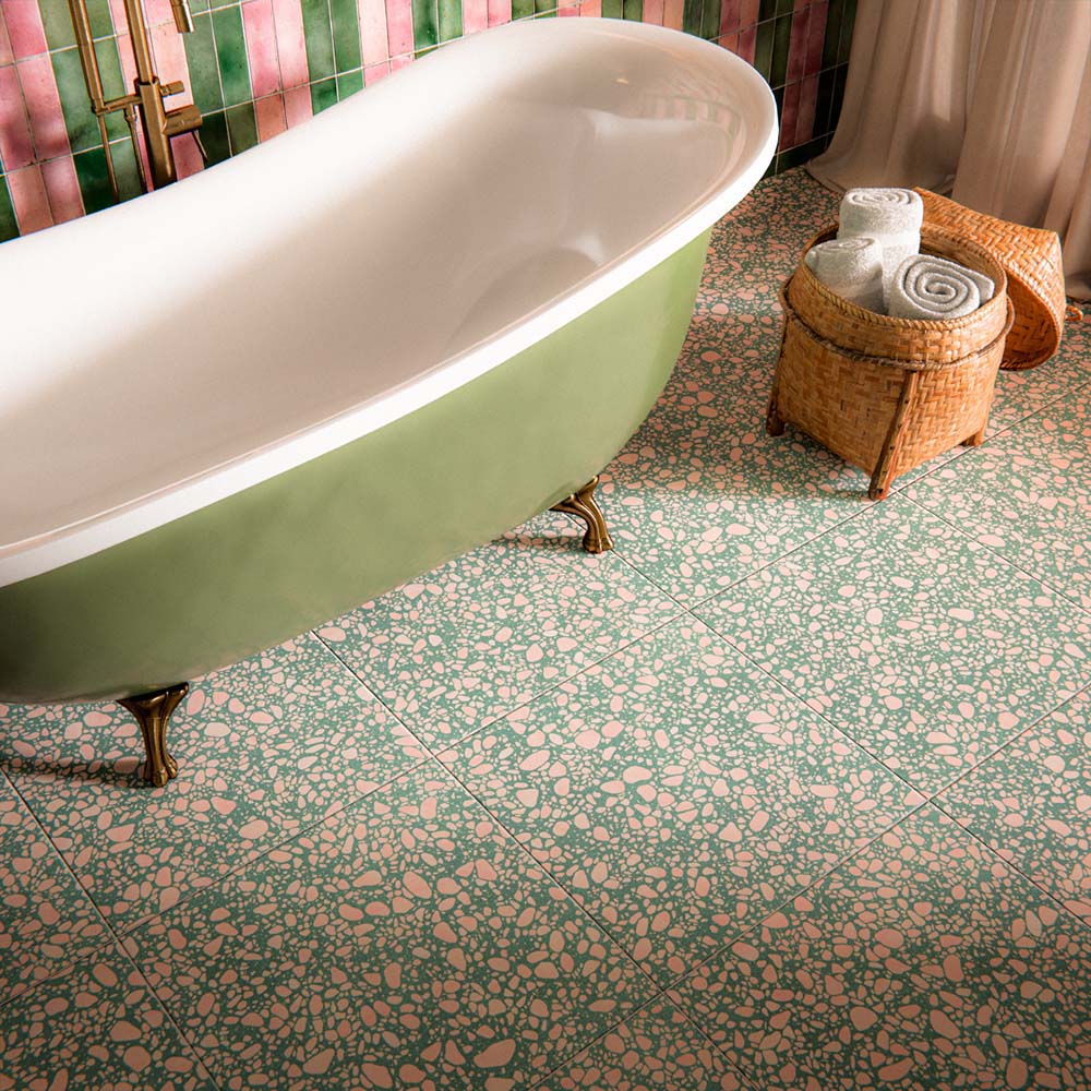 Bathroom featuring Melody POP Terrazzo Green 60 × 60cm terrazzo-effect porcelain floor tiles, showcasing a playful green and pink speckled design, paired with striped glossy wall tiles, floral wallpaper, and a sage green freestanding bath for a bold maximalist-inspired interior.