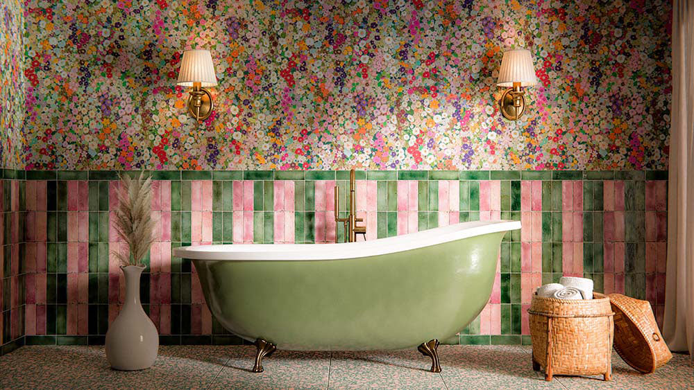 Bathroom featuring Melody POP Terrazzo Green 60 × 60cm terrazzo-effect porcelain floor tiles, showcasing a playful green and pink speckled design, paired with striped glossy wall tiles, floral wallpaper, and a sage green freestanding bath for a bold maximalist-inspired interior.