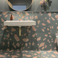 Bathroom featuring Melody ROCK Terrazzo Green 60 × 60cm terrazzo-effect porcelain wall and floor tiles, combining oversized blush pink stone fragments with a deep green base, paired with brass fittings and dark painted walls for a bold contemporary interior.