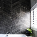 Lifestyle image of Monzo Stone Chevron Nite 10x53cm dark chevron porcelain wall tiles in deep charcoal tones, featuring subtle stone-effect texture and delicate veining, styled within a contemporary bathroom with dramatic contrast and modern black accents.