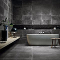 Lifestyle image of Monzo Stone Nite 30x60cm dark stone-effect porcelain wall and floor tiles, featuring rich charcoal tones, subtle veining and varied natural stone-inspired texture, styled within a contemporary bathroom with matte black accents and minimalist décor.
