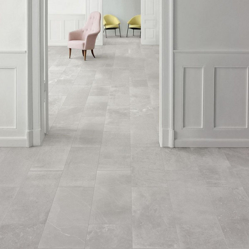 Interior featuring Monzo Stone Silver 30x60cm stone-effect porcelain floor tiles in soft silver-grey tones, styled with white panelled walls, pastel accent chairs, and subtle natural-style veining for a contemporary interior look.