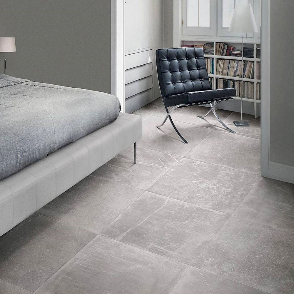 Bedroom featuring Monzo Stone Titanium 60x60cm stone-effect porcelain floor tiles in soft grey tones, styled with modern furniture, neutral interiors, black leather seating, and subtle natural-style veining.