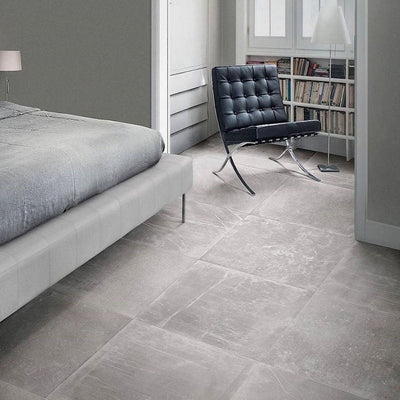 Bedroom featuring Monzo Stone Titanium 60x60cm stone-effect porcelain floor tiles in soft grey tones, styled with modern furniture, neutral interiors, black leather seating, and subtle natural-style veining.