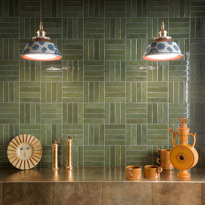 Contemporary kitchen splashback featuring Nomad Sage Green glossy brick wall tiles laid in a basketweave pattern, paired with bronze worktops, brass fittings, ceramic pendant lights and warm terracotta accessories for a rich, characterful interior.
