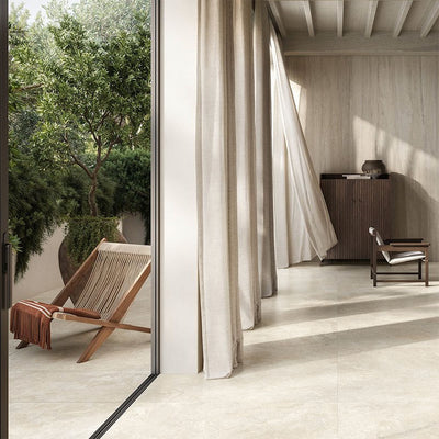 Living room featuring Nucetto Travertine 60x60cm wall and floor tiles, showcasing a soft travertine effect in warm cream and beige tones, extending seamlessly from the interior to the outdoor terrace for a calm, contemporary indoor-outdoor design.