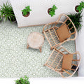 Outdoor patio seating area with rattan chairs, small round table and hanging plants, featuring London Streets Thornton Place Sage Green 20cm x 20cm Victorian Moroccan style patterned floor tiles in a fresh sage and white design.