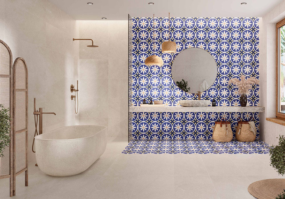 Bathroom featuring Peniscola Blue and Yellow patterned wall and floor tiles, showcasing a bold Mediterranean-inspired floral geometric design in vibrant cobalt blue, warm yellow and crisp white tones, paired with a floating stone vanity, round mirror, woven pendant lights, natural baskets and soft neutral finishes for a bright, characterful interior.