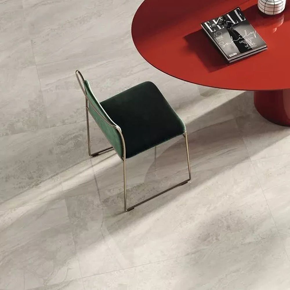 Close-up of Petra Beige stone marble effect porcelain wall and floor tiles in a 60cm x 120cm format, showcasing warm beige, ivory and soft cream veining inspired by natural stone, paired with a contemporary red statement table, green upholstered chair and elegant modern furnishings for a sophisticated interior.