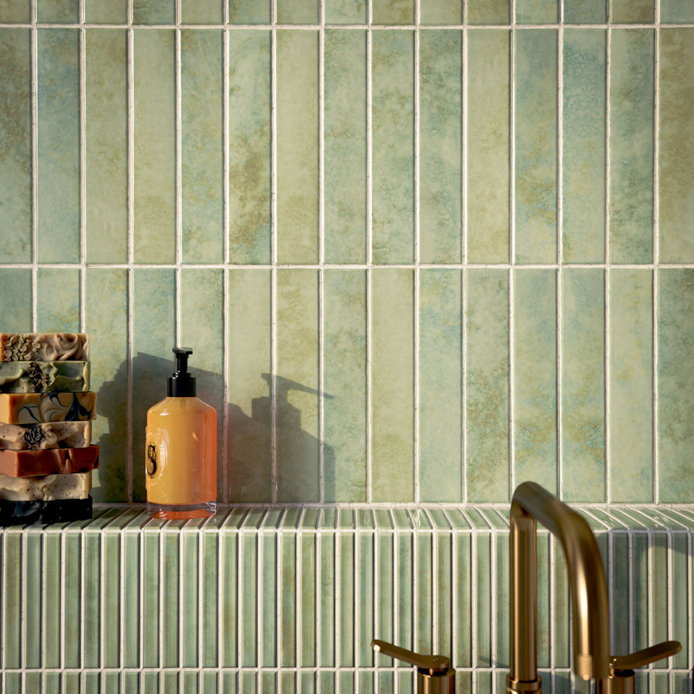 Bathroom featuring Pottery Agave Green 5x25cm glossy brick wall tiles with tonal variation, paired with striped tile detailing and brushed brass fixtures for a warm, spa-inspired contemporary interior.