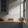 Kitchen splashback featuring Pottery Brick Blanco 5 × 25cm ceramic wall tiles, showcasing soft tonal variation, a glossy handcrafted finish, and a slim brick format, paired with deep blue cabinetry, warm wood worktops, and brass accents for a refined contemporary look.