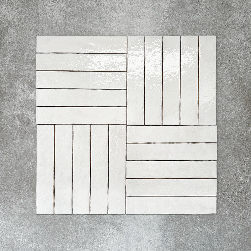Product display of Pottery Brick Blanco 5x25cm glossy wall tiles in soft white tones, arranged in a basketweave layout with handcrafted edges and subtle surface variation against a textured concrete-style backdrop.