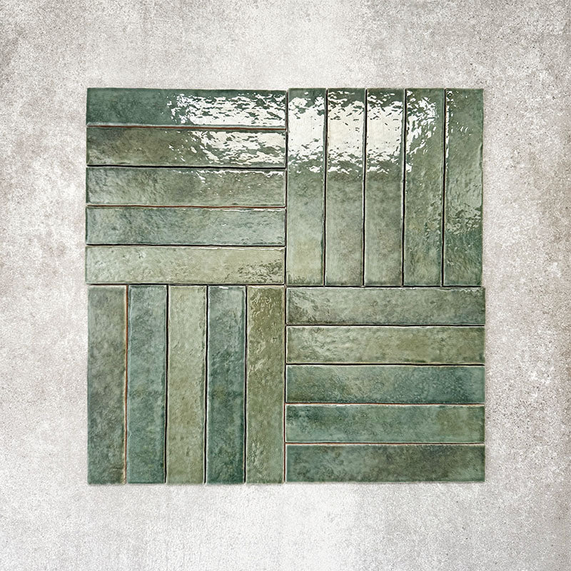 Product display of Pottery Brick Forest Green 5x25cm glossy wall tiles in deep green tones, arranged in a basketweave layout with handcrafted edges and rich tonal variation against a textured concrete-style backdrop.