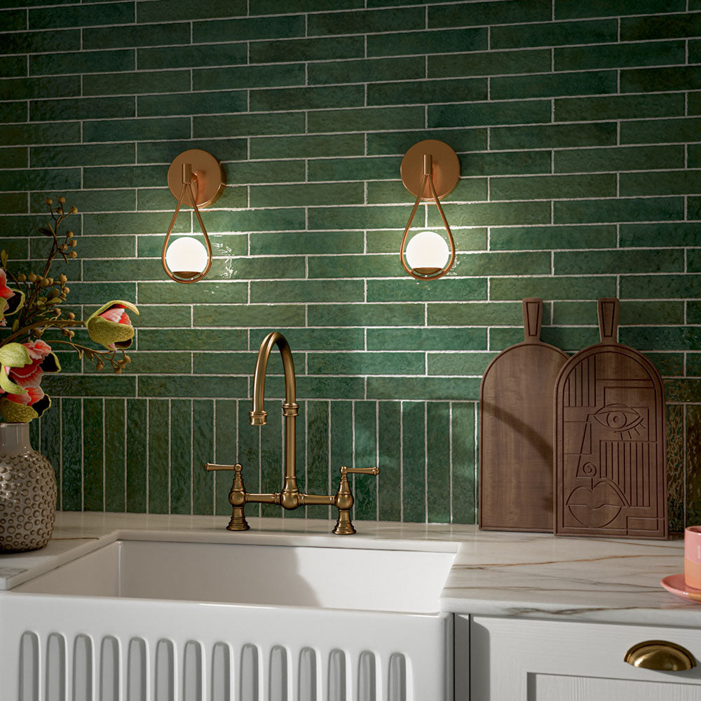 Kitchen featuring Pottery Forest Green 5x25cm glossy brick wall tiles, styled with cream shaker cabinetry, brass fixtures, a Belfast sink, and chequerboard floor tiles for a warm, vintage-inspired interior.
