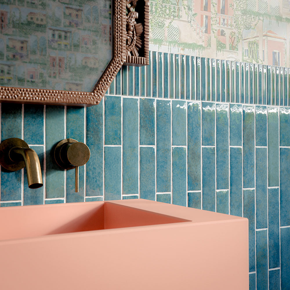 Bathroom featuring Pottery Prussian 5x25cm glossy brick wall tiles, styled with patterned wallpaper, a blush pink basin, and vintage-inspired brass fixtures for a bold, eclectic interior design.