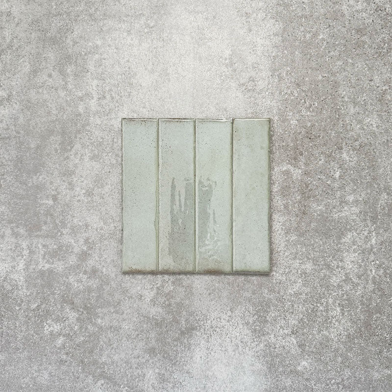 Product image of Puzzle Breeze Green Brick Rectified 5x20cm wall and floor tiles, featuring a glossy pale green finish with subtle tonal variation and softly aged edges, displayed to highlight the tile's handcrafted character.