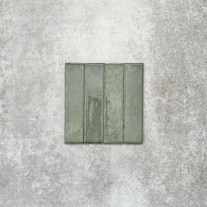 Product image of Puzzle Sage Green Brick Rectified 5x20cm wall and floor tiles, featuring a glossy sage green finish with subtle tonal variation and softly aged edges, displayed to highlight the tile's handcrafted character.