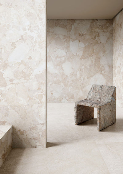 Interior featuring Riad Blanco Neutra Stone 30x60cm stone-effect wall and floor tiles, showcasing soft cream and beige tones with natural stone-inspired detailing, paired with a sculptural stone chair in a minimalist contemporary space.
