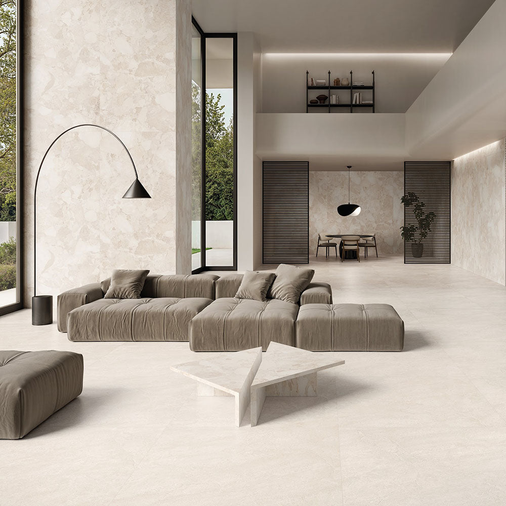 Contemporary living space featuring Riad Blanco Neutra Stone 60x60cm stone-effect wall and floor tiles, showcasing soft cream and beige tones, paired with minimalist furniture, floor-to-ceiling glazing and warm natural textures.