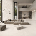 Contemporary living space featuring Riad Blanco Neutra Stone 60x60cm stone-effect wall and floor tiles, showcasing soft cream and beige tones, paired with minimalist furniture, floor-to-ceiling glazing and warm natural textures.