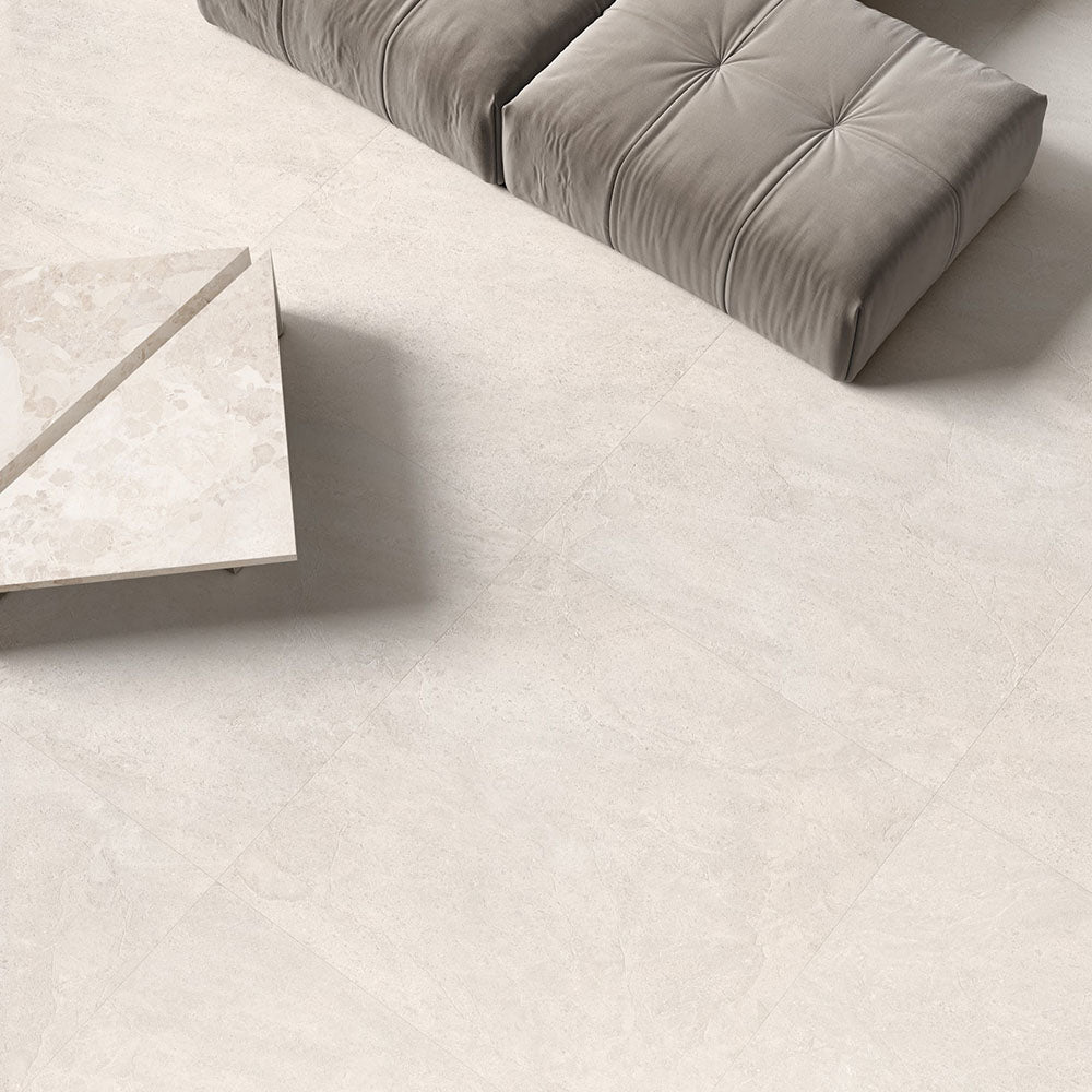 Contemporary living space featuring Riad Blanco Neutra Stone 60x60cm stone-effect wall and floor tiles, showcasing soft cream and beige tones, paired with minimalist furniture, floor-to-ceiling glazing and warm natural textures.
