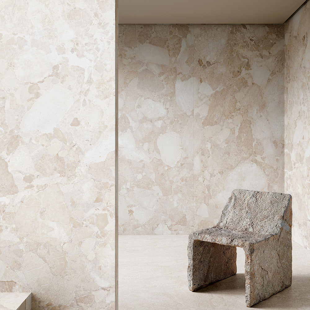 Interior featuring Riad Blanco Sassi Terrazzo Stone 60x60cm stone-effect wall and floor tiles, showcasing soft cream and beige tones with natural stone-inspired detailing, paired with a sculptural stone chair for a minimalist design.