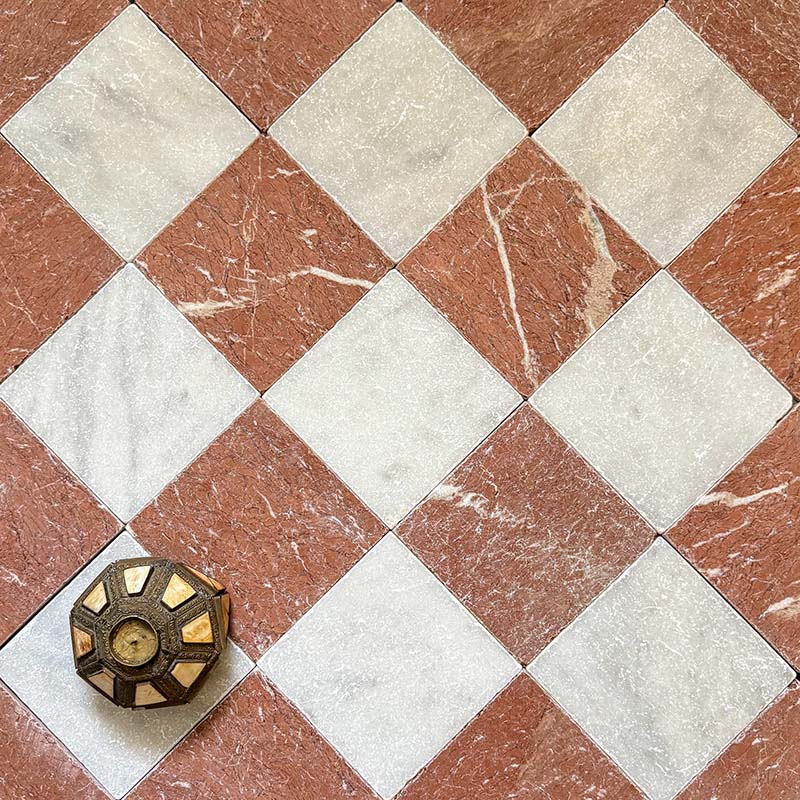 Chequerboard layout featuring Fayrouz Rosso 15.2x15.2cm natural marble tiles with a tumbled finish, paired with white marble tiles, installed diagonally and styled with a decorative object for added warmth and contrast.