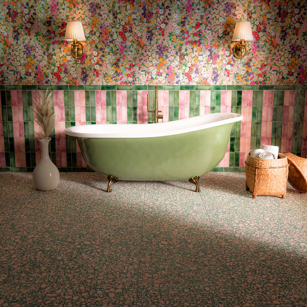 Bathroom interior featuring Foundry Bricks Coral Pink 6.5 x 20cm porcelain wall tiles, installed vertically alongside contrasting green tones to create a playful striped layout, paired with terrazzo effect floor tiles, floral wallpaper, and a freestanding bath for a bold, characterful space.