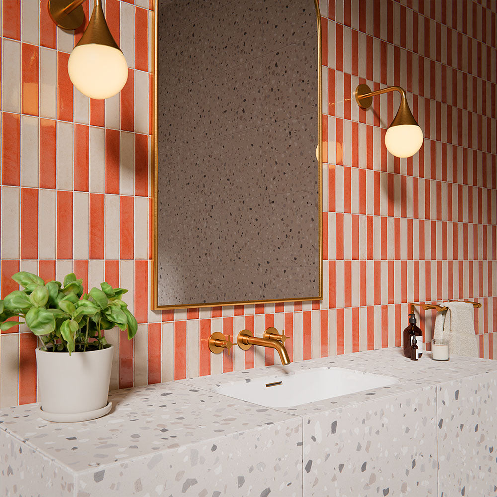 Puzzle Coral Brick Rectified 5x20cm wall and floor tiles in a vertical stacked layout, featuring warm coral and white tones in a contemporary bathroom setting with terrazzo vanity and brass fixtures.