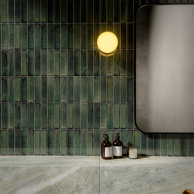 Bathroom interior featuring Puzzle Forest Green Brick rectified wall and floor tiles in 5x20cm format, installed vertically as a textured feature wall above large-format marble-effect tiles, styled with brass fittings and modern basin.