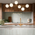 Puzzle Breeze Green Brick Rectified 5x20cm porcelain wall and floor tiles styled across a curved kitchen island and splashback, showcasing soft breeze green tones with subtle speckling and gentle shade variation. The elongated brick format enhances the island’s rounded form, while pairing beautifully with warm wood cabinetry, marble worktops and brushed brass fixtures for a calm, contemporary finish.