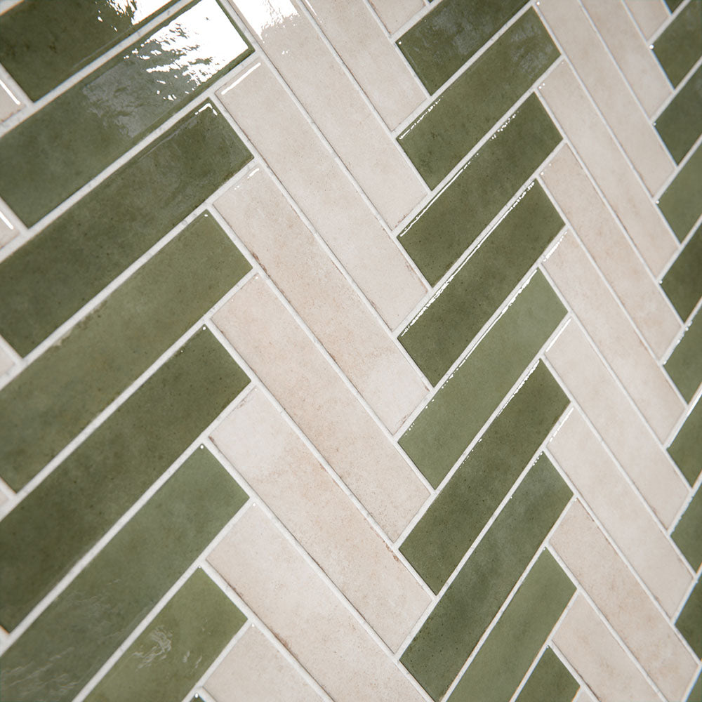 Bathroom interior featuring Nomad Sage Green and Nomad Oatmeal 6 x 24.6cm industrial style brick tiles, arranged in a striking herringbone pattern to create a layered, textural wall design, paired with a natural stone bath and soft neutral flooring for a calm, contemporary finish.