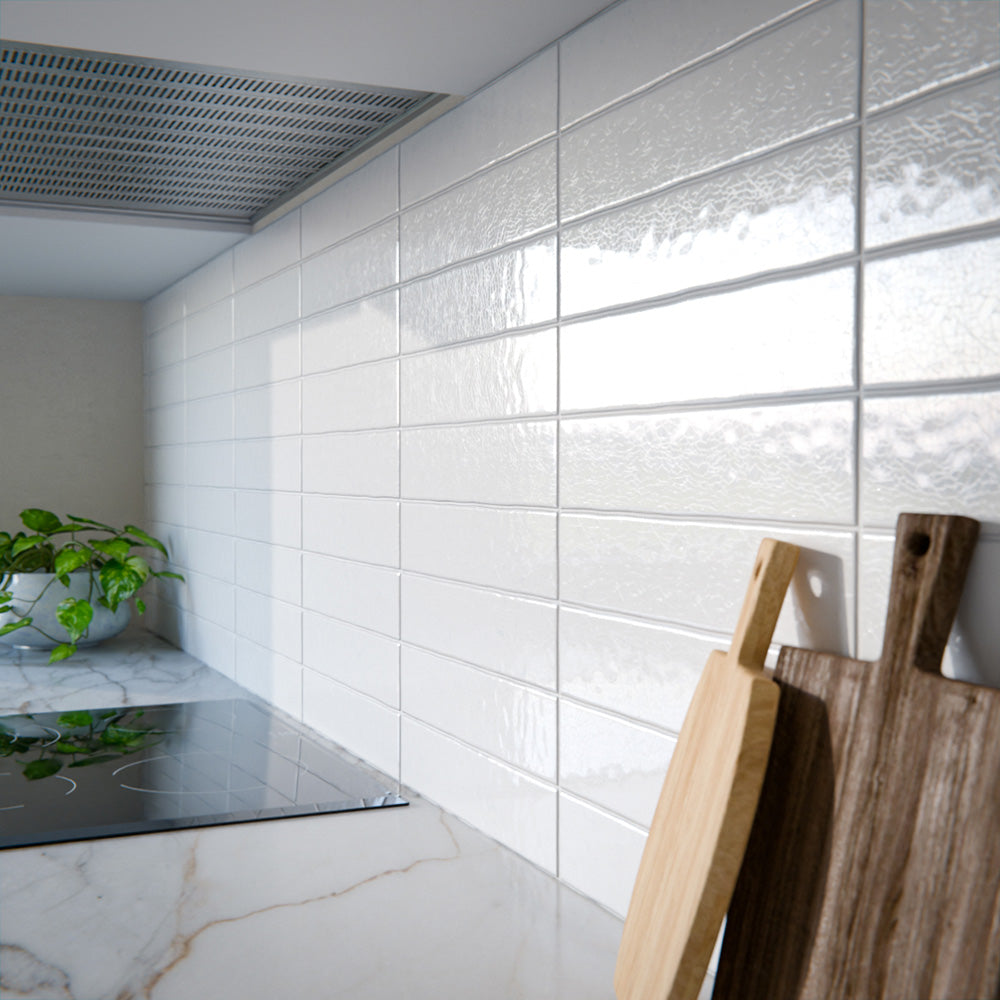 Modern kitchen featuring Bora Bora White Sand Brick ceramic wall tiles in a 6.5 × 32.8cm slim brick format with a flux glaze finish, laid horizontally as a splashback behind blue cabinetry, paired with white worktops, open shelving, and brass tapware for a clean, contemporary look.
